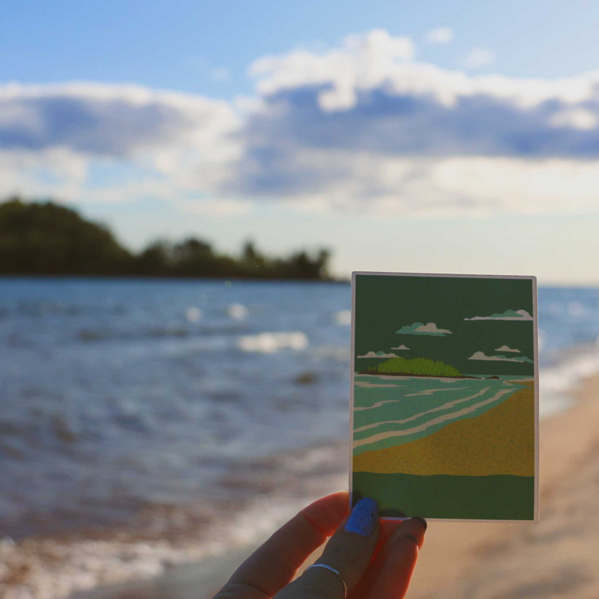 a hand holding a piece of paper on a beach