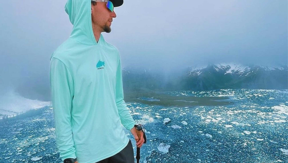a man in a hoodie and sunglasses standing in front of a snowy landscape